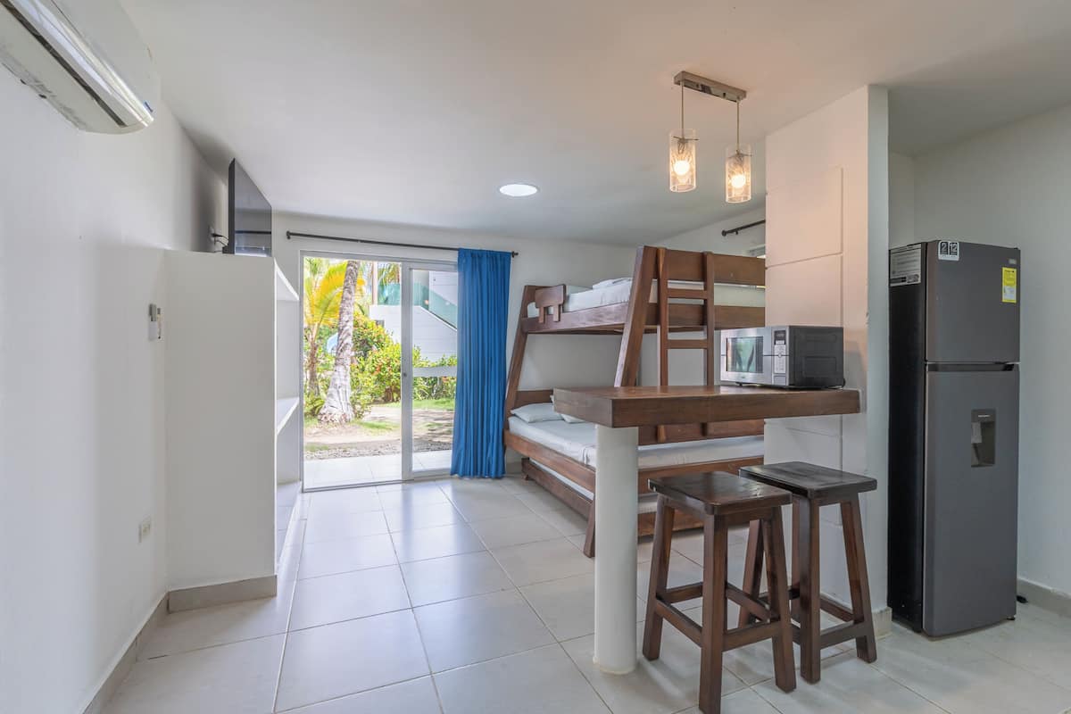 A compact room with a bunk bed, a kitchenette with a refrigerator and microwave, and a sliding glass door leading to an outdoor area.