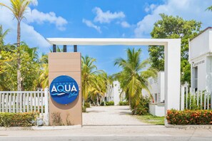Une entrée fermée par un portail, sur laquelle on peut lire l’inscription « AQUA Blue », et un bâtiment blanc doté d’un toit plat.