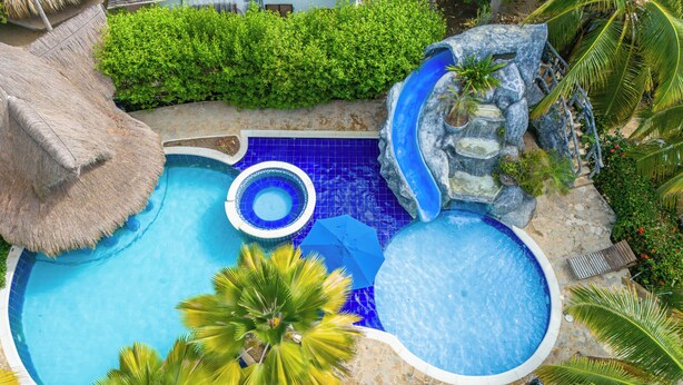 A swimming pool with a hot tub, a thatched roof, and surrounding greenery. - Cabañas Aqua Blue Coveñas (Coveñas)
