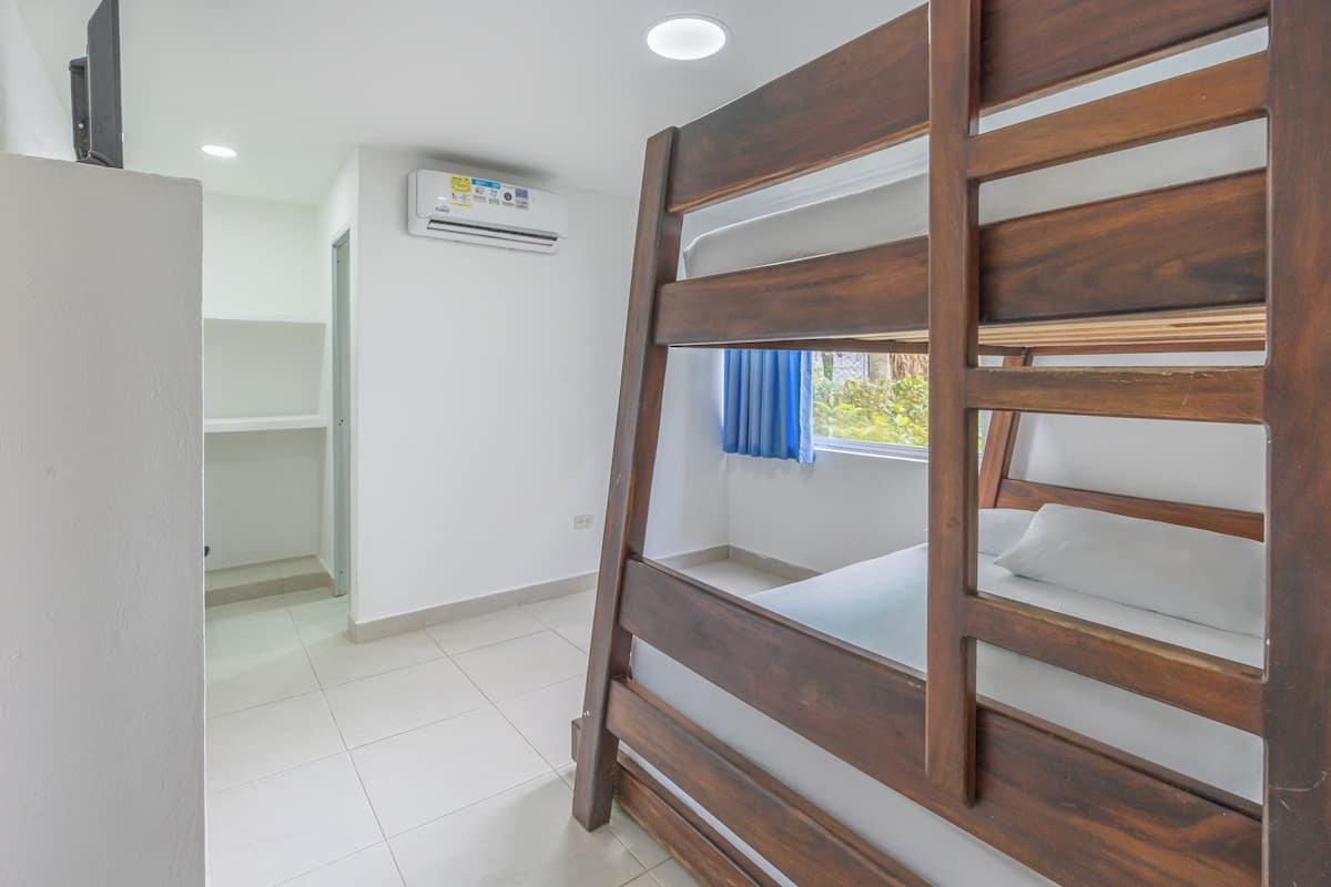 A bunk bed with a wooden frame, a white mattress, and a window with blue curtains.