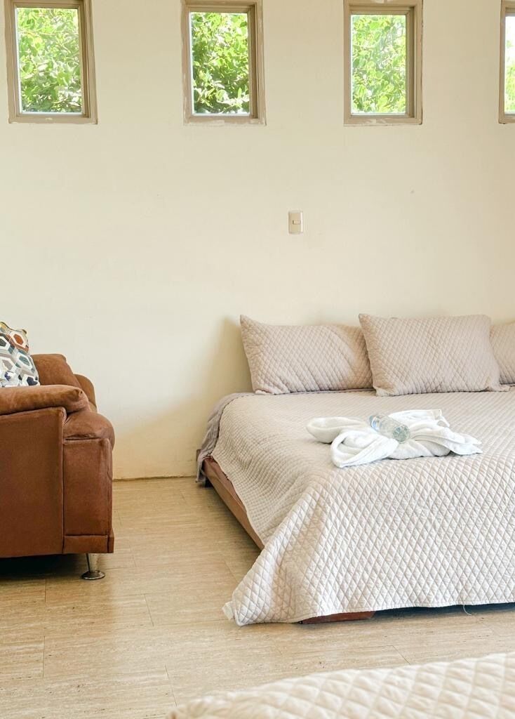 Un dormitorio con cama, sofá marrón y tres ventanas.