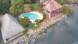 Vue aérienne d’un complexe hôtelier comprenant une piscine, une structure à toit de chaume et un bâtiment avec un toit rouge.