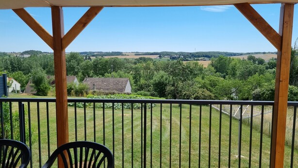 A covered outdoor area with a view of a green landscape and distant buildings. - Quiet country house (Triguères)