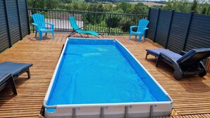 A rectangular inflatable pool on a wooden deck with blue chairs and lounge chairs, surrounded by a black fence. - Quiet country house (Triguères)