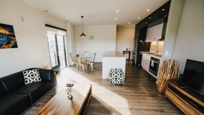 Un salon moderne avec une table basse en bois, un canapé noir et un coin repas avec des chaises.