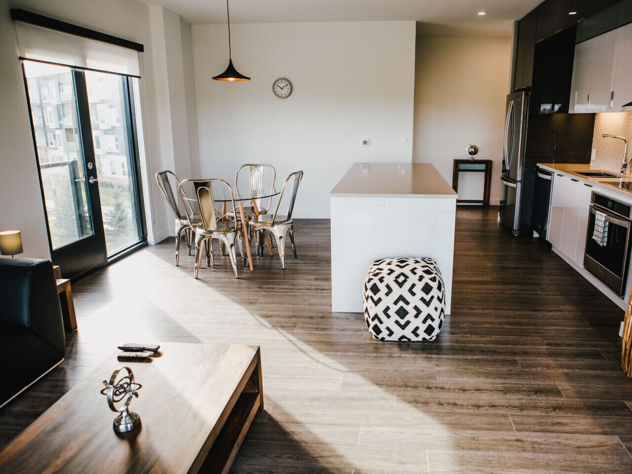 A modern kitchen with dark wooden floors, a central island, and a dining area with chairs and a table.