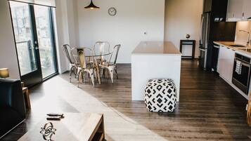A modern kitchen with dark wooden floors, a central island, and a dining area with chairs and a table.