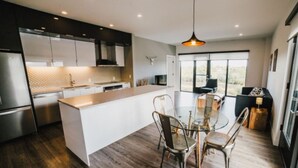 Une cuisine moderne dotée d’un îlot central, d’appareils électroménagers en acier inoxydable et d’un coin repas avec une table en verre et des chaises en métal.