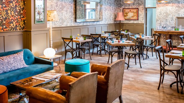 A spacious lounge area with multiple seating options, including sofas and chairs, and a dining area with tables and chairs. - Moore House (Hastings)