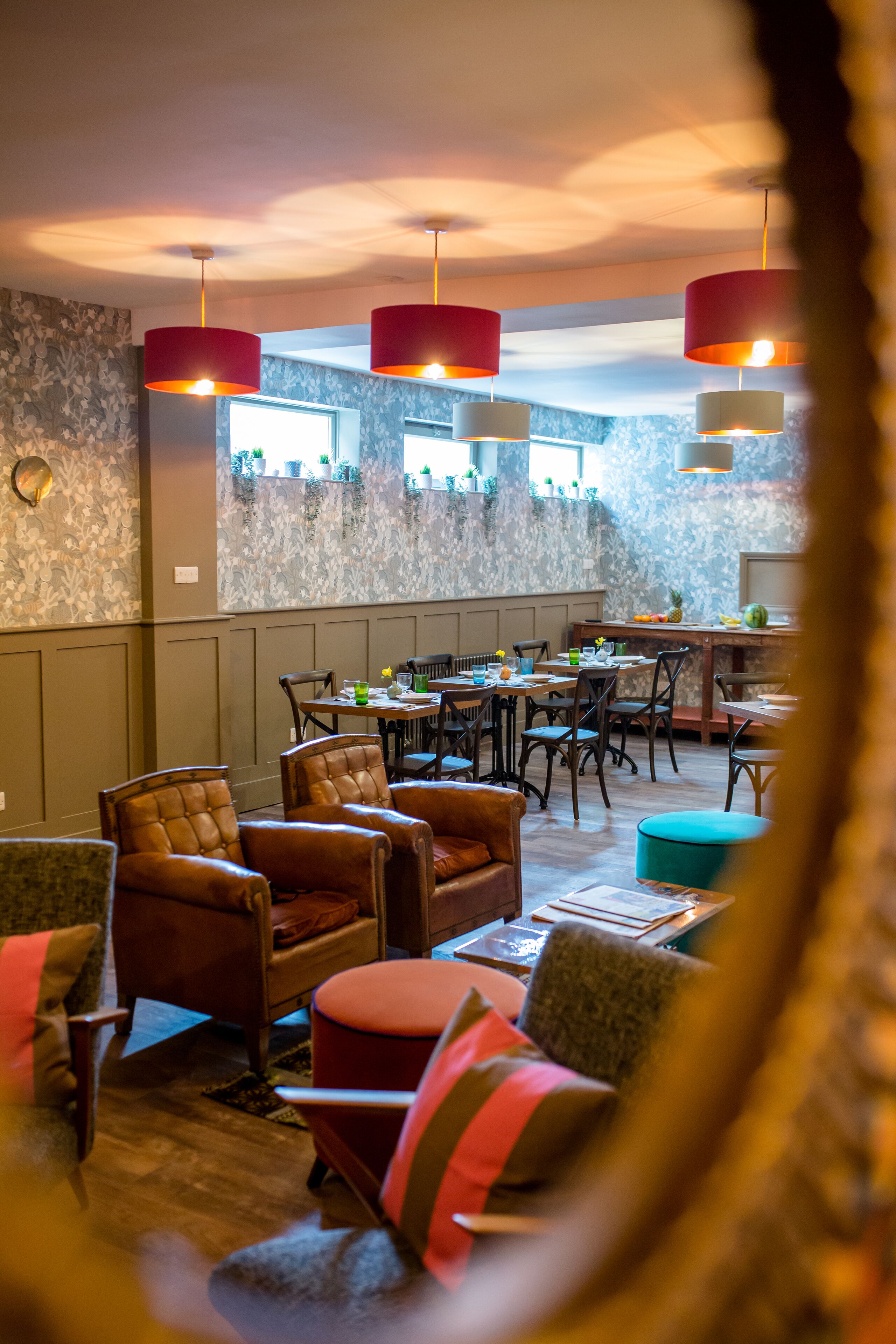 A restaurant with wooden furniture, red and white pendant lights, and a stone wall.