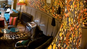 A cozy lounge area with a patterned wall, a sofa, a small table, and a radiator. - Moore House (Hastings)