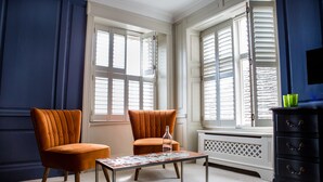 A room with two orange chairs, a table with a magazine, and a dark dresser with green glasses on top. - Moore House (Hastings)