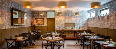 A restaurant with wooden tables and chairs, hanging pendant lights, and a bar area.