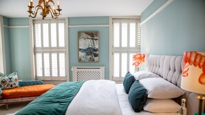 A bedroom with a large bed, a chaise lounge, a chandelier, and a painting on the wall. - Moore House (Hastings)