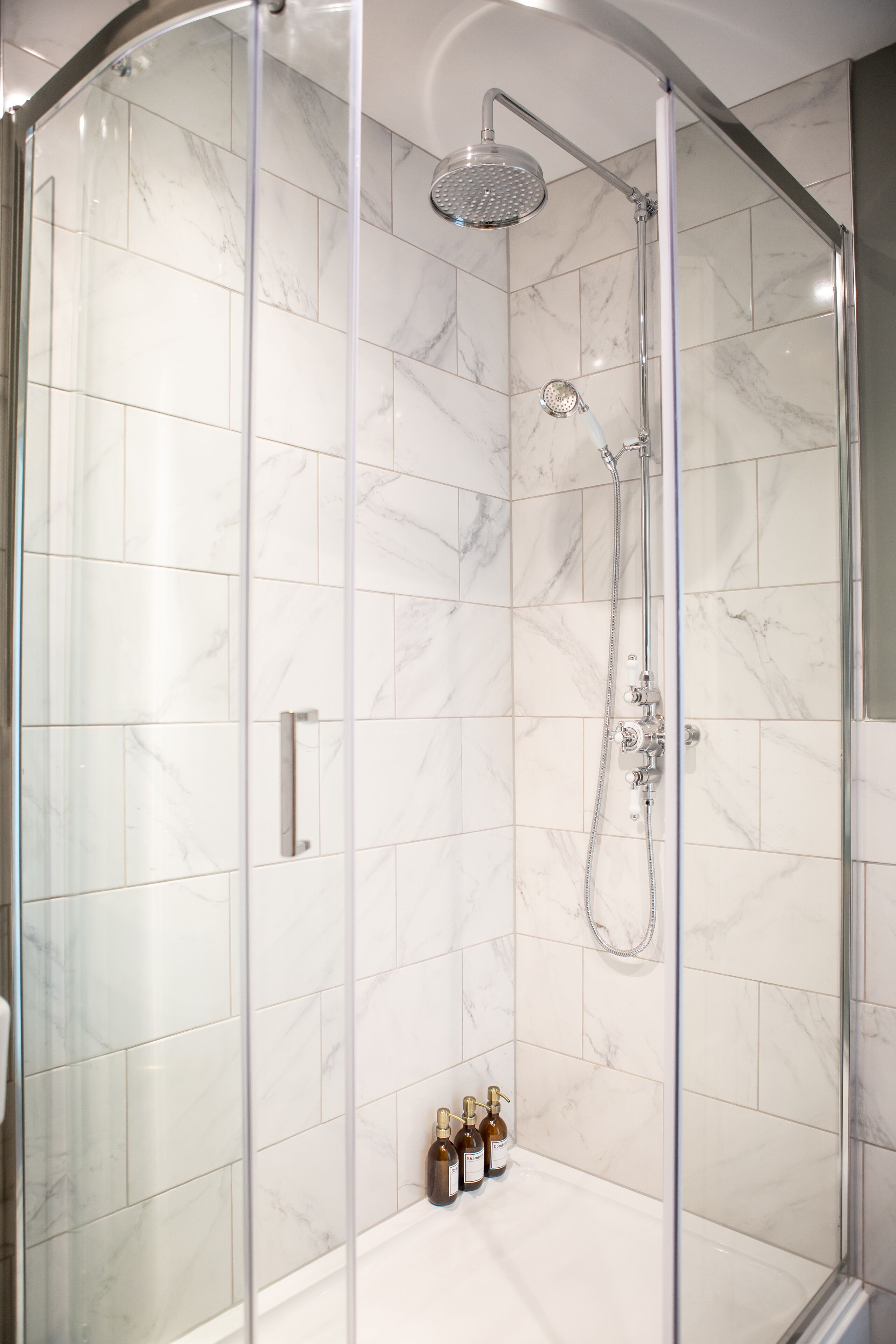 A glass-enclosed shower with a handheld showerhead and a wall-mounted faucet.