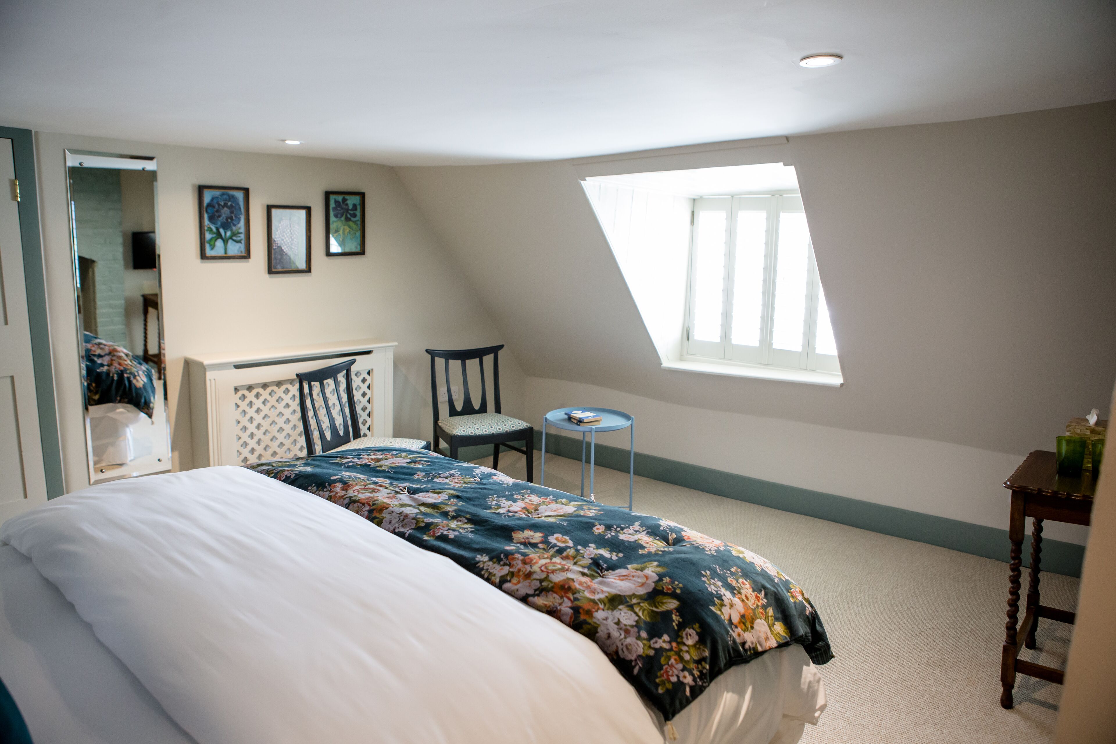 Ein Schlafzimmer mit einem großen Bett, einem kleinen Tisch, zwei Stühlen, einem Fenster und einem Spiegel.
