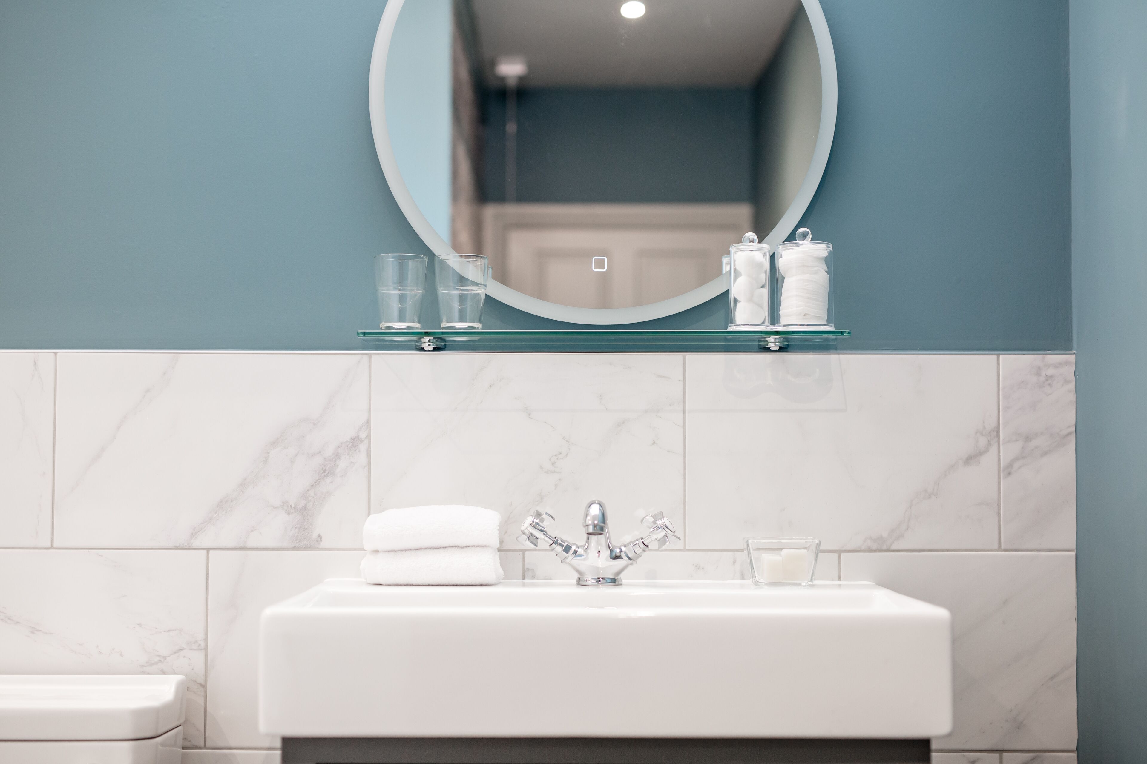 Un baño con un lavamanos blanco, un espejo y un estante de vidrio encima.
