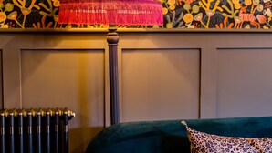 A room with a patterned wallpaper, a green sofa with a leopard print pillow, and a radiator. - Moore House (Hastings)
