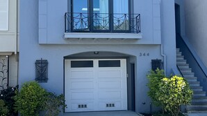 Een modern huis met twee verdiepingen, een garage, een balkon met metalen hekwerk en een trap naar de tweede verdieping.
