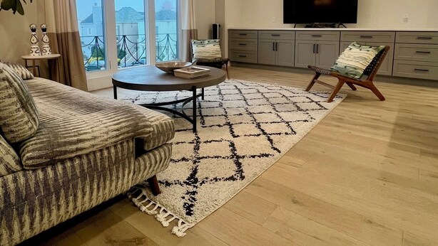 Een ruime woonkamer met een bank, een salontafel, een vloerkleed met dessin, een televisie, en een balkon met uitzicht.