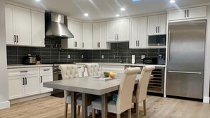 Een moderne keuken met witte kasten, een roestvrijstalen koelkast, en een eethoek met een tafel en stoelen in een lichte kleur.