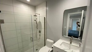 Een moderne badkamer met een douchecabine van glas, een wit toilet en een wastafel met spiegel.