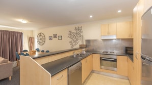 A compact kitchen with a dishwasher, stove, and refrigerator. There is a dining area with a table and chairs. - Silvertrees - 2/1 McLure Cir (Jindabyne)
