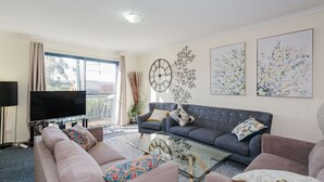 A modern living room with a sofa set, a glass coffee table, and a large wall clock. - Silvertrees - 2/1 McLure Cir (Jindabyne)