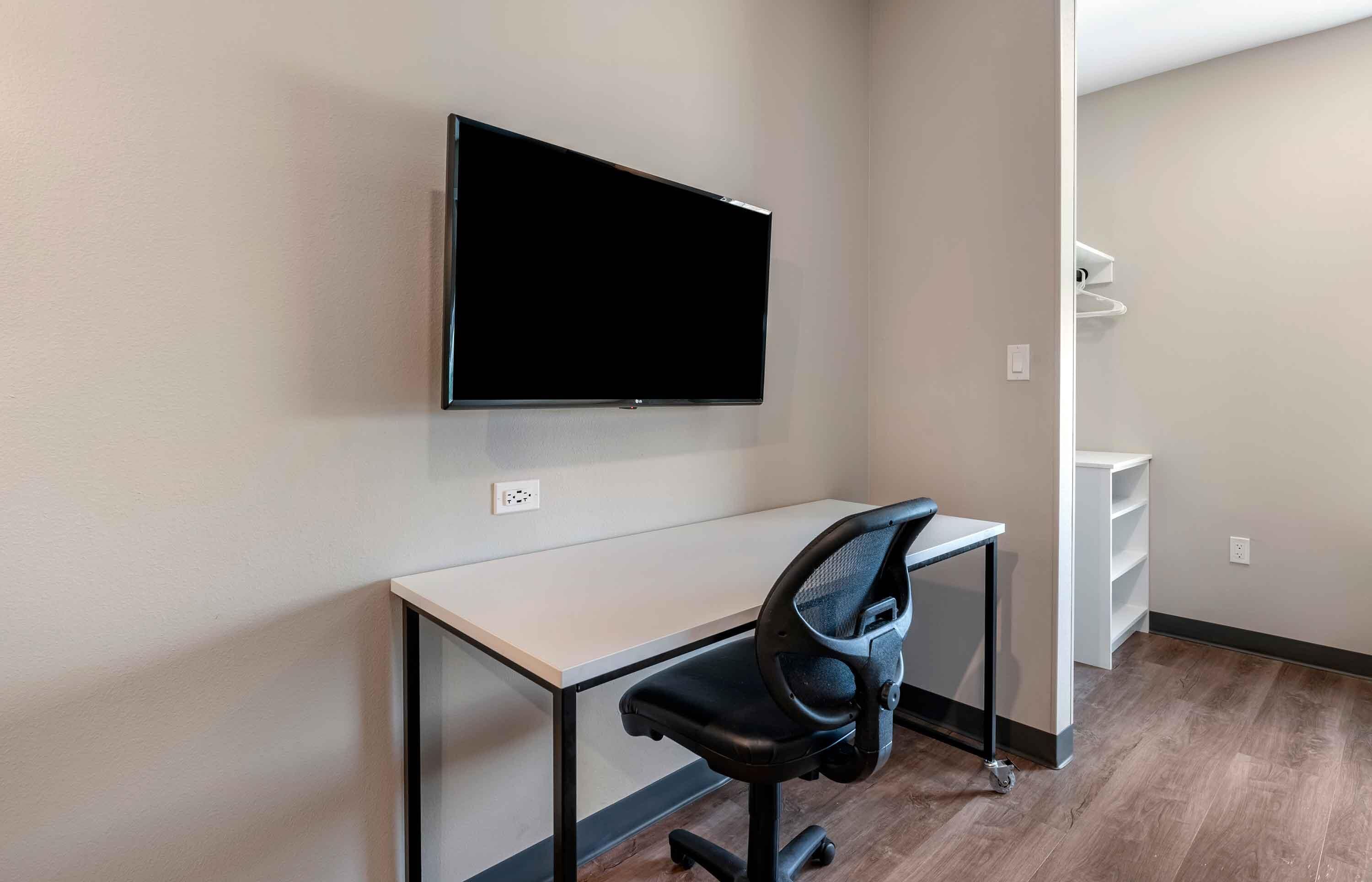 Espaço de escritório moderno com televisão de tela plana fixada na parede, uma mesa e uma cadeira de escritório preta.