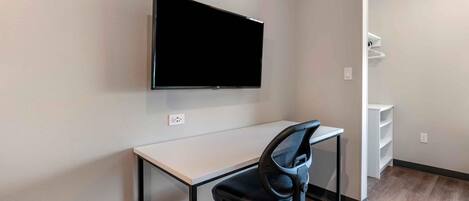 Espaço de escritório moderno com televisão de tela plana fixada na parede, uma mesa e uma cadeira de escritório preta.