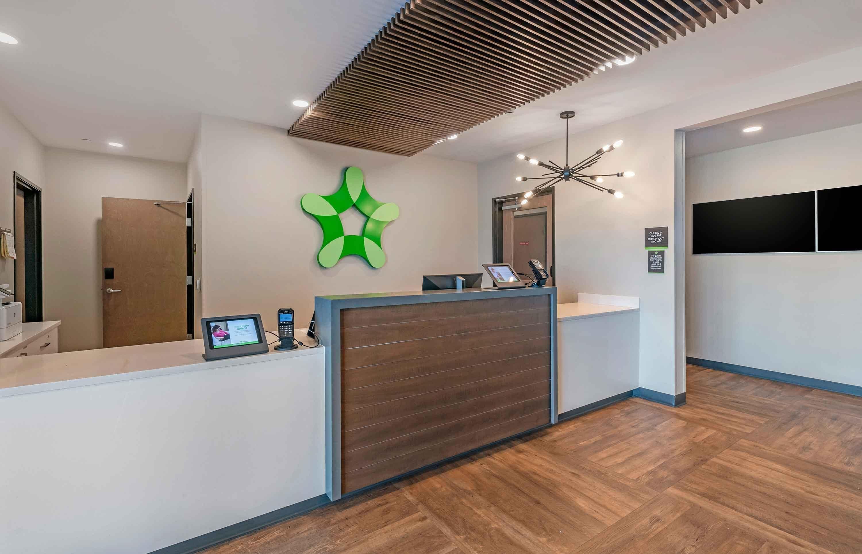 A reception area with a wooden reception desk, a green abstract wall art, a modern ceiling design, and a mounted TV.