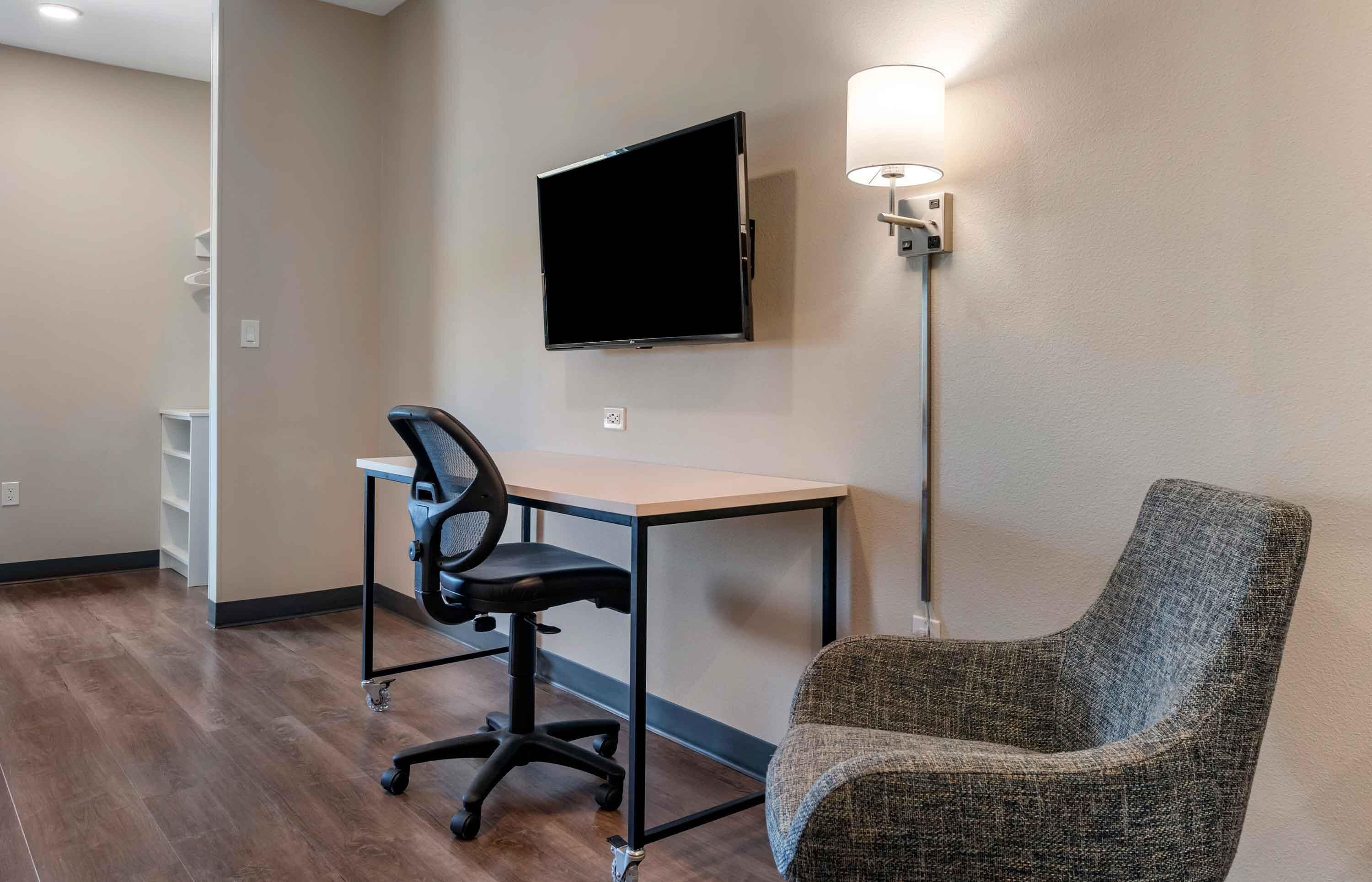 A room with a desk, office chair, television, and a lamp.