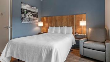 Habitación de hotel con una cama grande, dos mesitas de noche, una silla, un cabecero de madera y un cuadro colgado en la pared.
