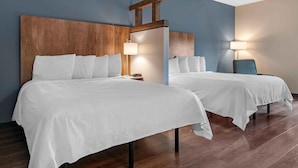 Een hotelkamer met twee bedden, houten hoofdeinden, bedlampjes en een houten vloer.
