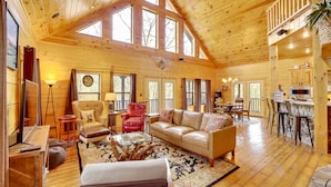 A spacious wooden cabin with a high ceiling, large windows, a cozy living area with a sofa and armchairs, a dining area, and a kitchen. - Spacious & Secluded Cabin: 25 Mi to Bentonville! (Sulphur Springs)