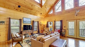 A spacious living room with wooden walls and floors, a large sofa, a television, and a deer mounted on the wall. - Spacious & Secluded Cabin: 25 Mi to Bentonville! (Sulphur Springs)