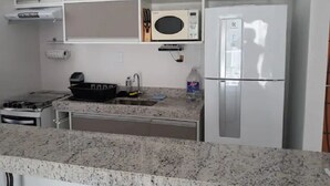 Una cocina con encimera de granito, microondas, estufa, refrigerador y armarios.