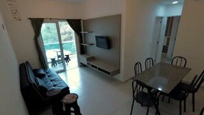Una sala de estar con sofá, una mesita, televisor montado en la pared y un comedor con mesa y sillas.