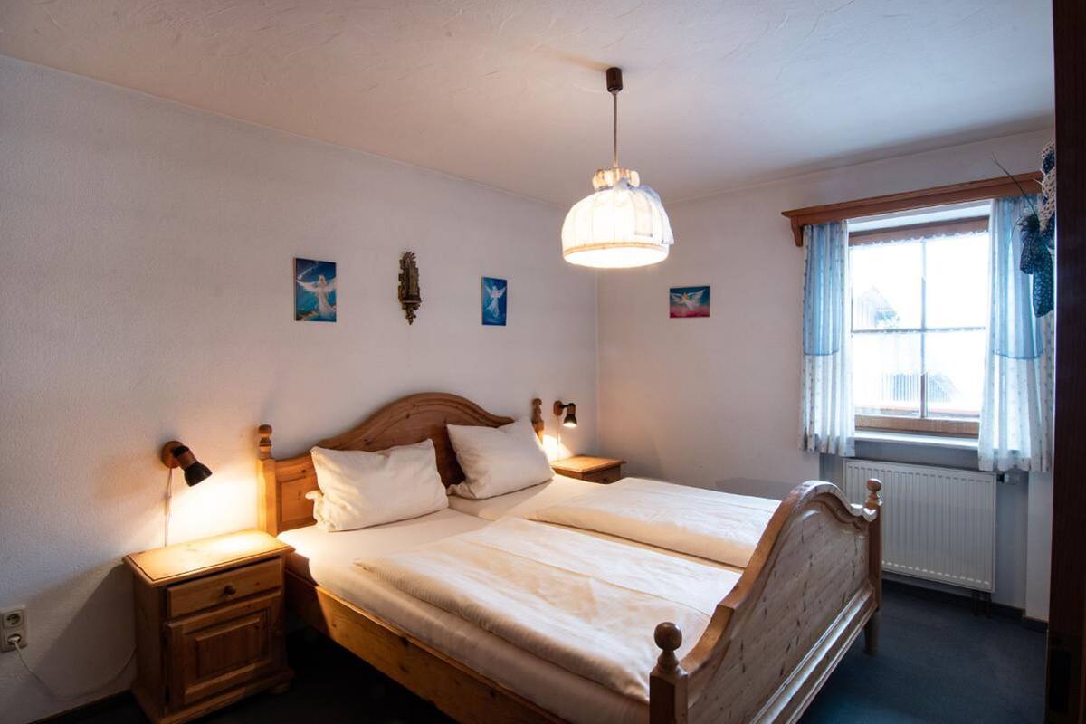 Une chambre à coucher avec un lit double, des tables de chevet, un luminaire suspendu et une fenêtre avec des rideaux.