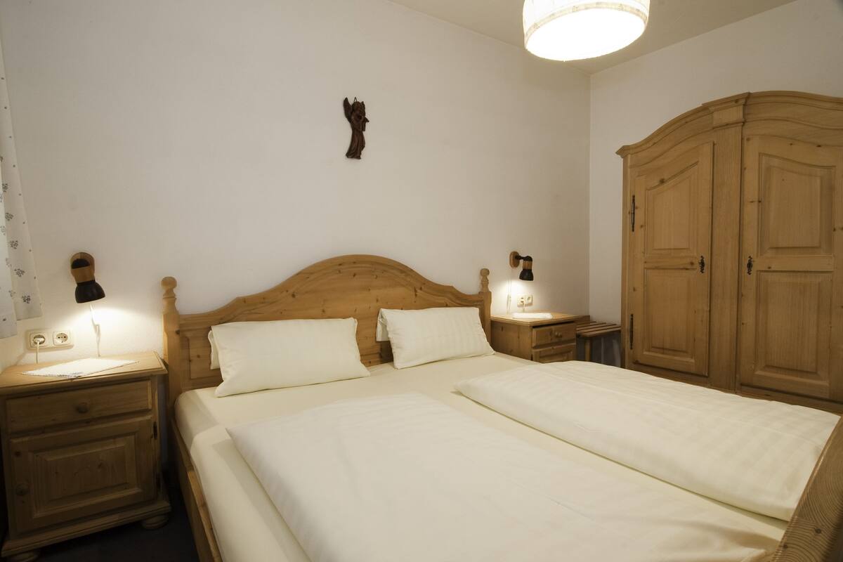 Une chambre à coucher avec un lit en bois, deux tables de chevet, une commode, une armoire et un luminaire fixé au mur.