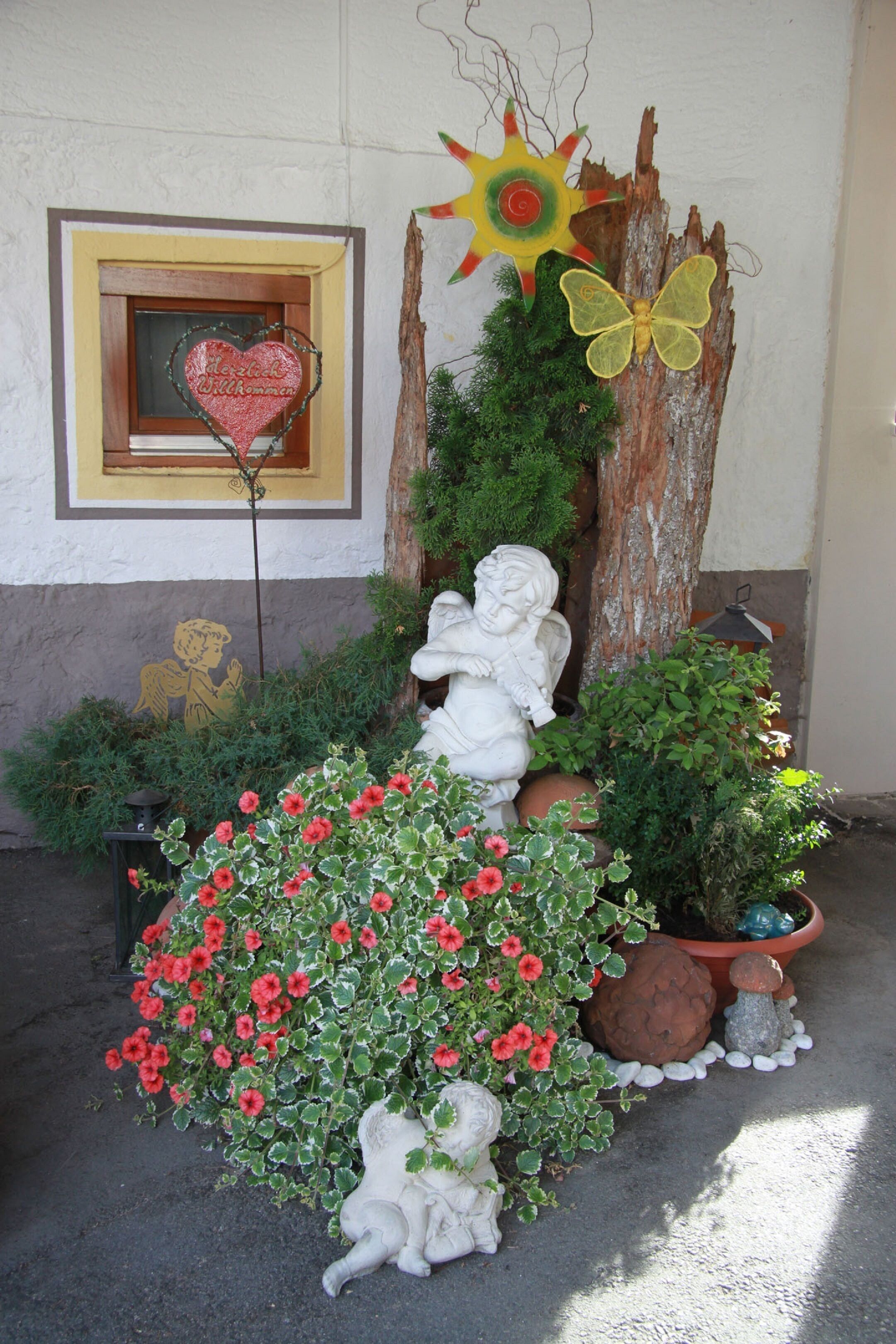 Un espace extérieur décoratif agrémenté d’une enseigne en forme de cœur, d’une statue de putin et de diverses plantes, notamment des fleurs rouges et une plante en pot.