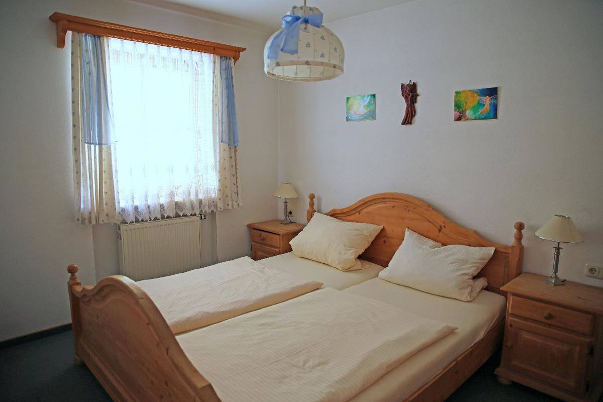 Un lit double avec deux tables de chevet, une fenêtre avec des rideaux, un radiateur et deux œuvres d’art murales.