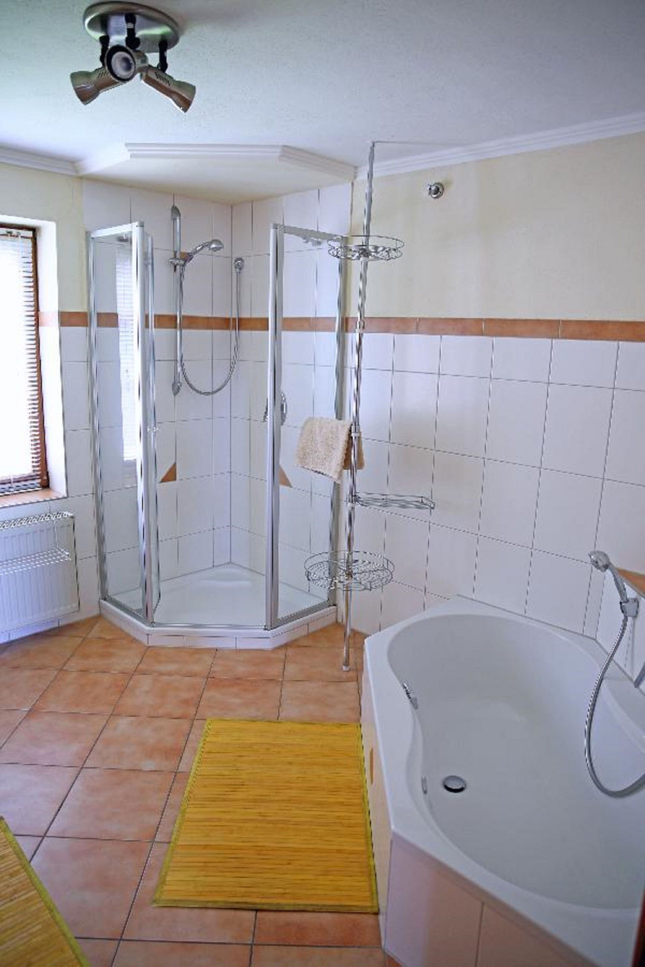 Un baño con ducha envuelta en vidrio, una bañera y un tapete amarillo en el suelo.