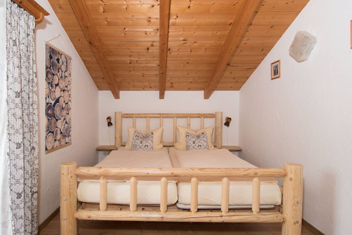 Un lit en bois avec une tête de lit, deux oreillers et un matelas, dans une pièce dont le plafond est orné de poutres en bois.