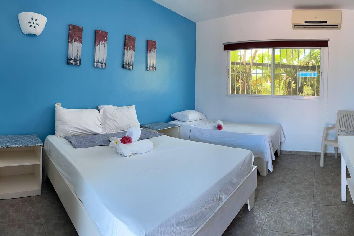 Une chambre d’hôtel avec deux lits, un bureau, une chaise et une fenêtre donnant sur un espace verdoyant.