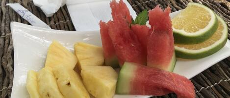 A plate with pineapple chunks, watermelon slices, and lime halves on a woven tablecloth.