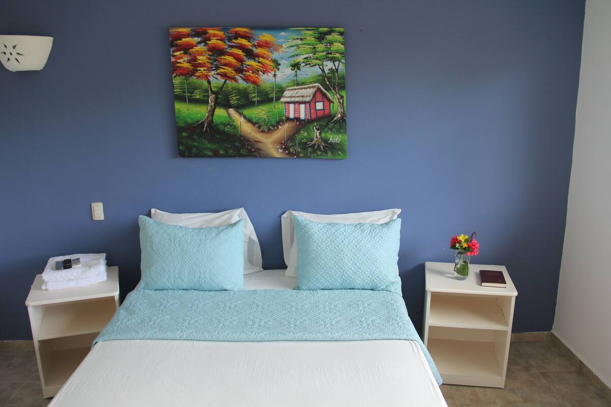 Une chambre à coucher avec un lit, deux tables de chevet, un tableau et un vase de fleurs.