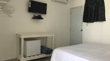Ein Schlafzimmer mit einem Bett, einem an der Wand montierten Fernseher, einer kleinen weißen Kommode und einer Tür mit Vorhang.