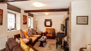 A cozy living room with a fireplace, a sofa set, a television, and a stone wall. - The Old Farmhouse (Burgpreppach)