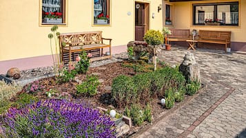 Een binnentuin met stenen bestrating, houten banken en diverse planten, waaronder paarse bloemen.